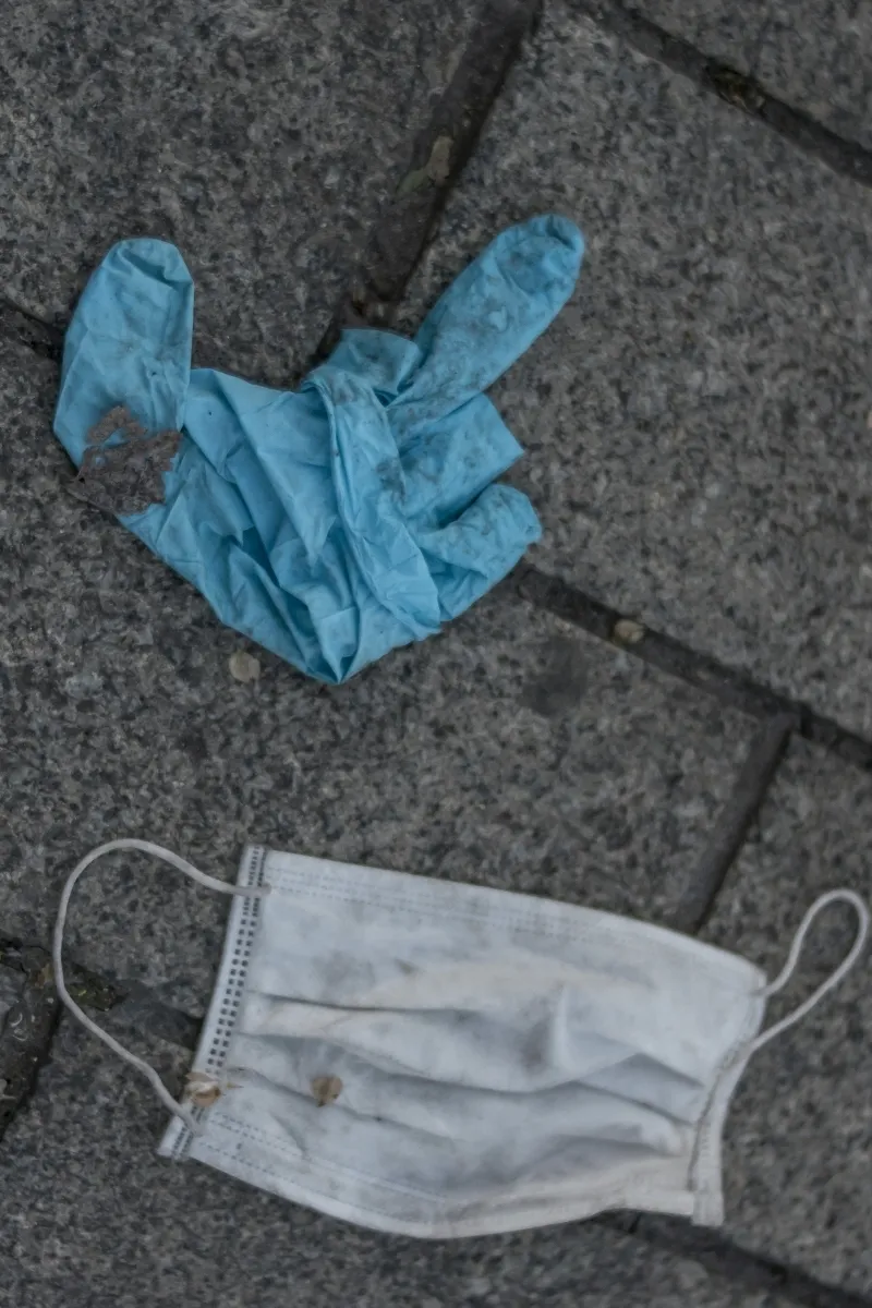 Blue rubber glove lying above a dirty disposable face mask on paving stones